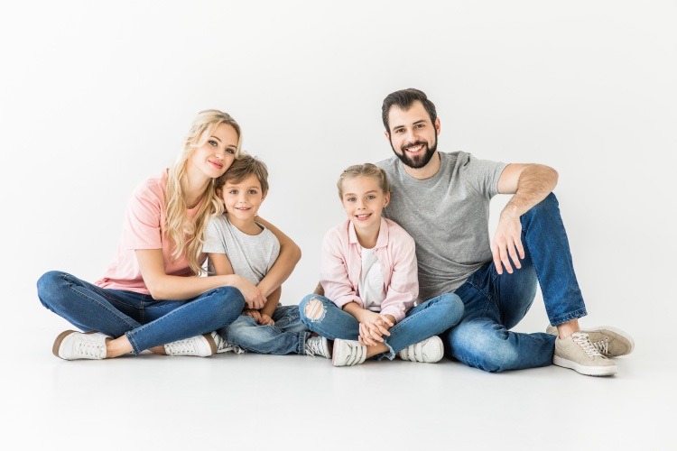 A mom and dad smile while sitting on the floor with their son and daughter at the dentist in Prairie Village, KS