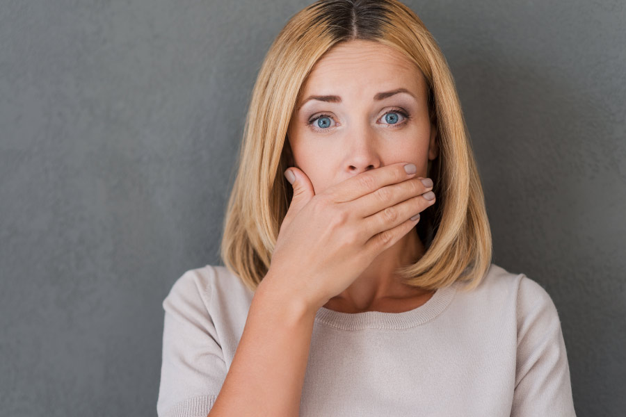 Photo of a blond woman covering her mouth for fear of bad breath.
