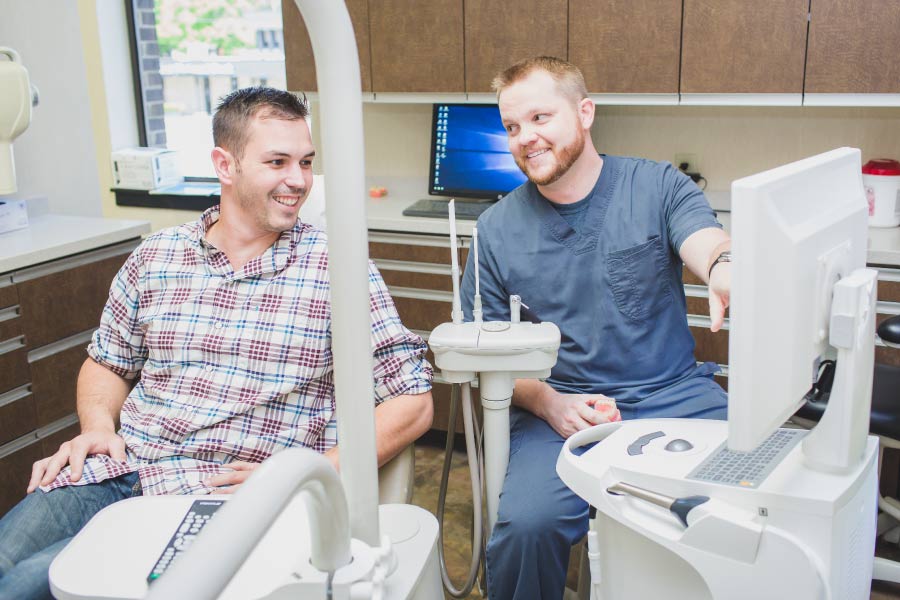 Doctor Chaney discusses treatment with a male patient in the dental chair.