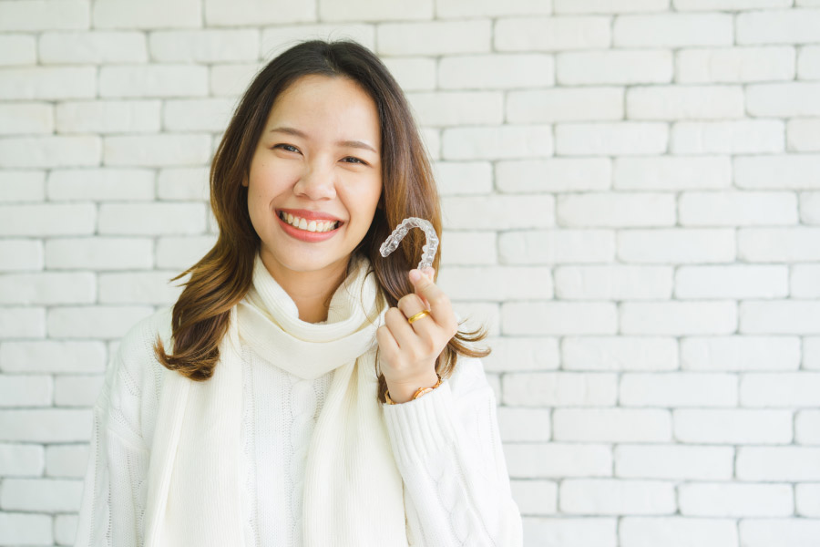 Smiling young woman holding a clear aligner.